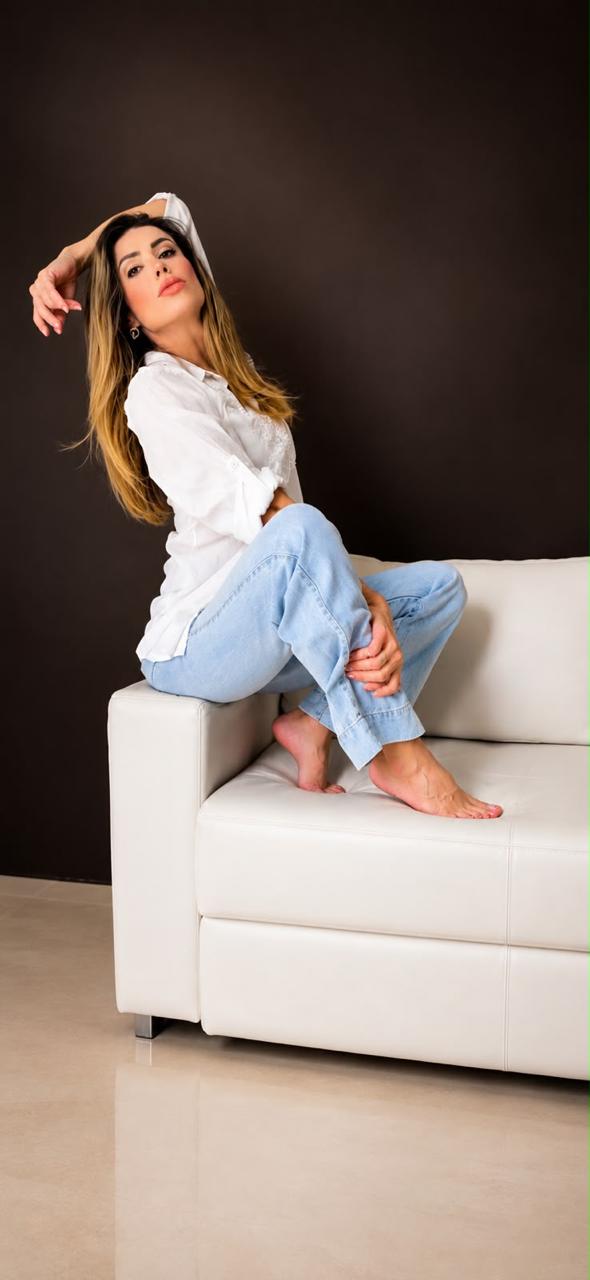 Lorena de camisa branca e jeans, sentada em um sofá